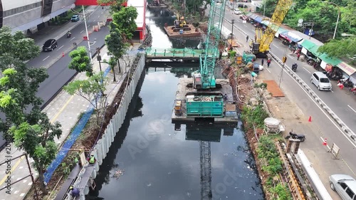 Sustainable Urban Planning for Future Cities Aerial view of bridge foundation construction on a river, featuring heavy steel sheet piling, concrete reinforcement, and a tall tower crane on a cofferdam