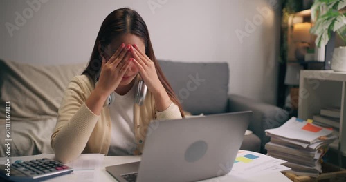 Stressed Asian female entrepreneur with headache during work at home. Burnout, overwork, financial stress, and deadline pressure.