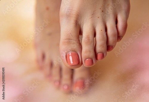 Close-up of woman's feet with coral toenail polish, soft pink background