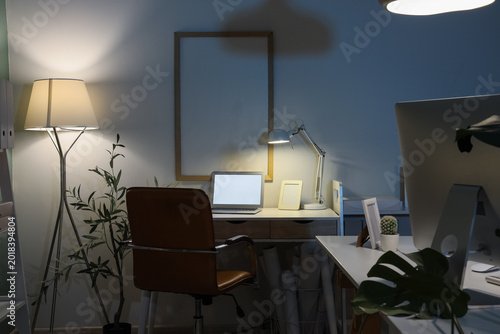 Fotografi Interior of dark office with desks and glowing lamps at night