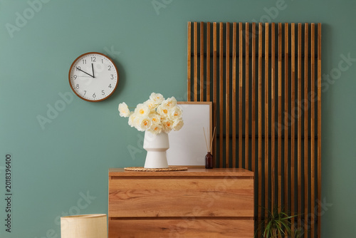 Schilderij op canvas Vase with artificial white flowers on commode near green wall in room