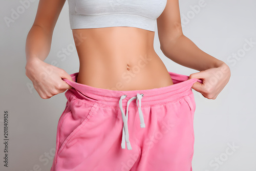 Close up of slim woman pulling her loose pink waistband symbolizing diet achievement
