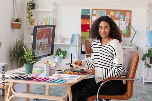 Female African-American interior designer with color palettes at table in office