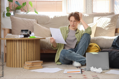 Upset male student with paper studying at home
