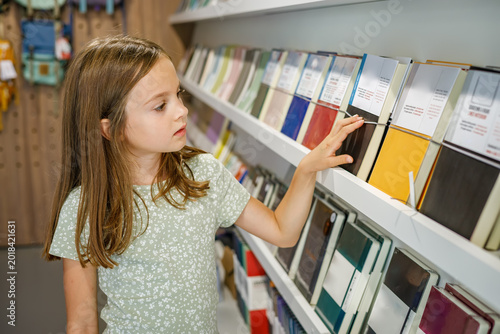 Young girl choosing a notebook or diary from a shelf in a stationery store or bookstore during back to school shopping season