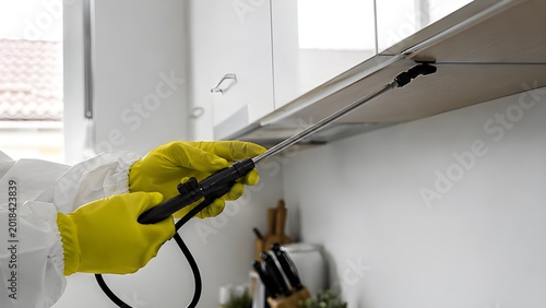 Pest Control Technician Hands Spraying Kitchen Cabinets in Modern Luxury Home Wearing Protective Hazmat Gloves for Residential Exterminator Service and Professional Pest Management Treatment