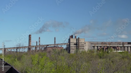 Wide panorama of industrial factory complex with smokestacks, industrial buildings and heavy industry infrastructure surrounded by green vegetation. 4K industrial landscape footage.