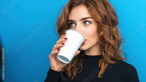 Slow zoom tracking shot woman sipping coffee from takeaway cup in studio with blue background
