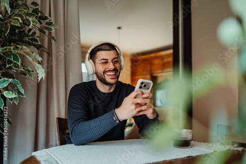 Happy man wearing headphones using smartphone at home