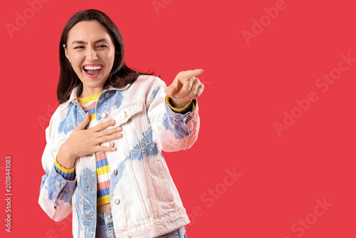 Bild auf Leinwand Laughing young woman pointing at viewer on red background