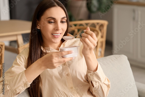 Young woman eating tasty yoghurt at home, closeup
