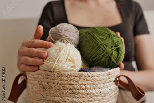 Hands gently hold a woven basket filled with colorful yarn. The warm light illuminates a serene indoor setting, inspiring creativity and relaxation