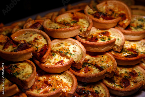 Pile of mini savory quiches with cheese and meat on a catering tray