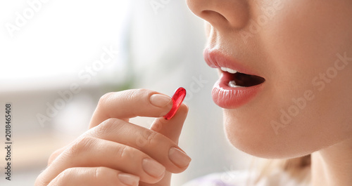 Woman taking vitamin E pill at home, closeup