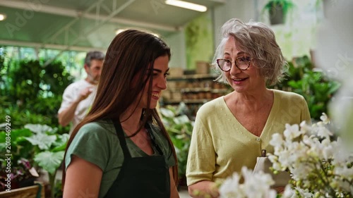 Young female florist helping elderly customer choose orchid in a flower shop