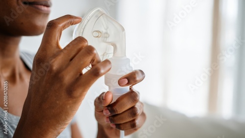 A woman using an inhaler to manage her respiratory health, holding the device in her hands with a determined look on her face.