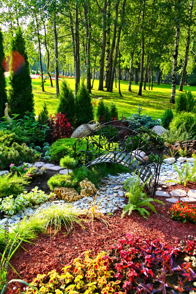 Obraz premium Serene Garden with Lush Greenery and Decorative Stone Path in Sunlit Forest Park