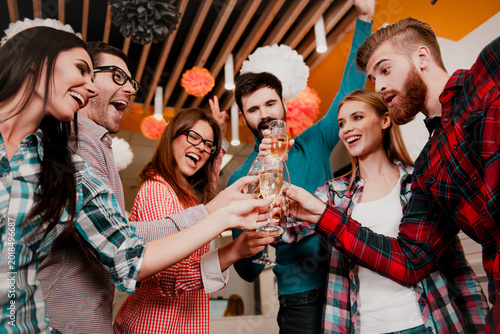 Fotografie Group of friends toasting with champagne at a casual indoor party, laughing, cel