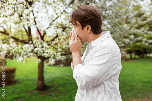 Foto A man sneezes into a tissue while standing near blooming trees in a park