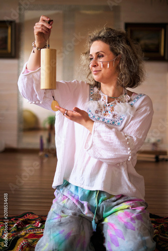 Bilde på lerret Portrait of a female wellness guide gently presenting a hanging chime while seated indoors on a woven rug