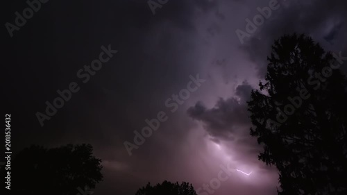 Series of lightning bolts on a dark night sky above the silhouette of trees, captured in slow motion.