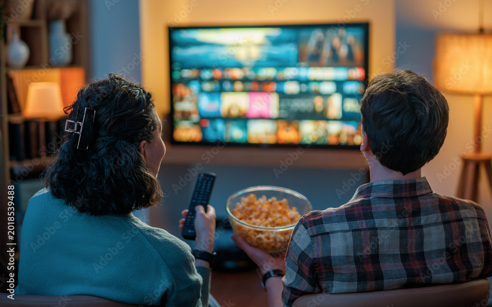 Obraz premium Couple Enjoying Movie Night at Home Watching Streaming TV and Ea