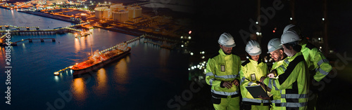 Tableau sur toile Yellow Coveralls Inspect Large Oil Refinery Cargo Ship Docked in Dark Harbor Amidst Concrete Piers, Examining Vessel at Port Facility for Inspection Operations