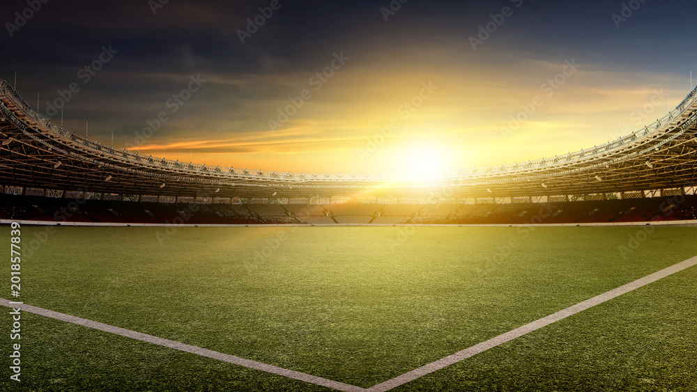 Obraz premium A wide-angle view of a professional football stadium at sunset. The empty arena features a lush green field under a dramatic golden hour sky with a bright lens flare