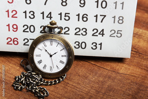 The calendar and pocket watch are on the wooden table.Time is money.