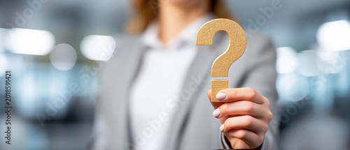 Businesswoman hand holding question mark symbol focus communication, blurred office background soft light selective