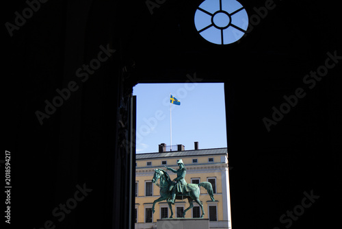 Photography Statue of king on horse framed by dark archway with national flag in Stockholm S