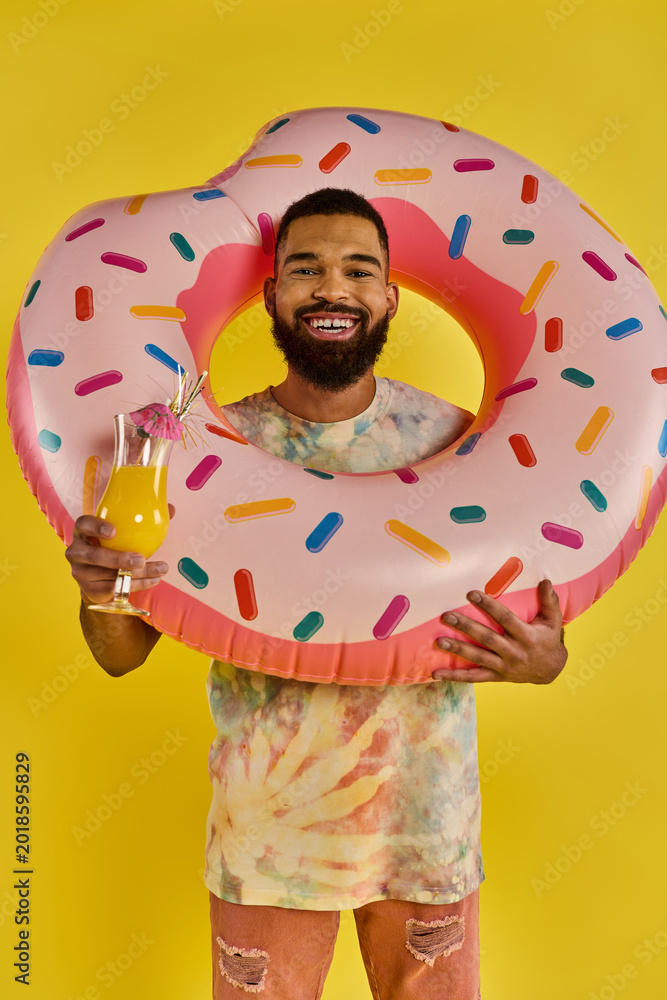Fototapeta premium Vibrant young man enjoying a sunny day with a playful donut float and refreshing drink
