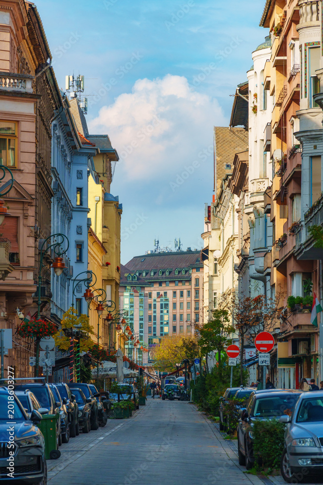 Obraz premium Beautiful street view in Budapest city with historic colorful buildings and parked cars under a blue sky with white clouds during a bright sunny day in Hungary