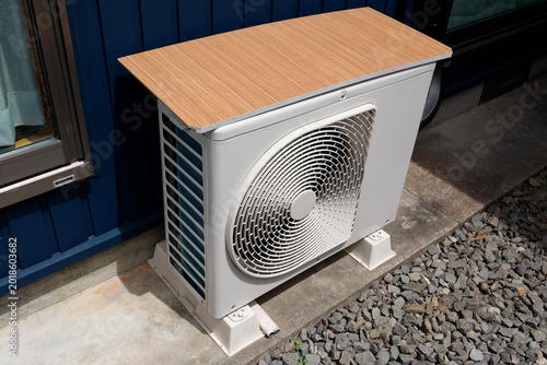 エアコン室外機。暑さ対策で上に木製板を載せている。白色機器。