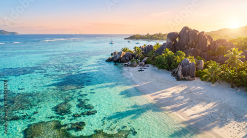 Idyllic tropical beach with turquoise water, granite boulders, and lush green palm trees under a golden sunset sky.