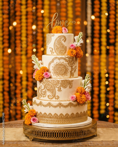 Four tier wedding cake with golden paisley henna patterns and orange marigold flowers