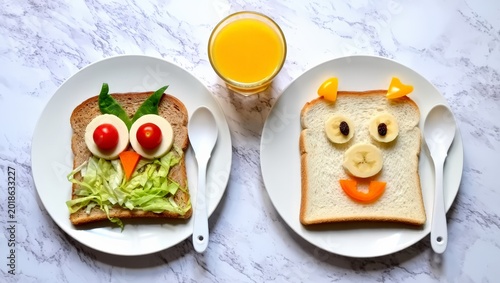 A creative and playful breakfast setup for kids featuring food art on toast and a glass of orange juice on a marble table, promoting a fun and healthy meal experience.