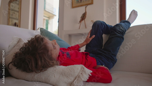 Εκτύπωση καμβά Child resting comfortably on sofa while gazing out window with peaceful expressi