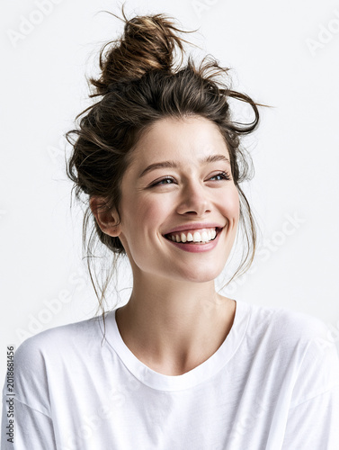 Joyful young woman with a messy bun hairstyle laughing heartily against clean white studio background.
