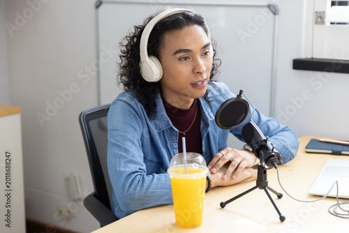 Non-binary person wearing denim shirt, white headset speaking into mic with pop filter in studio