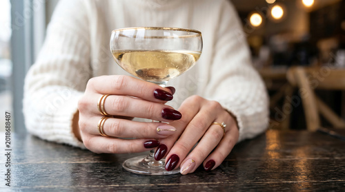 Woman holding a glass of champagne with elegant manicure and rings in a restaurant