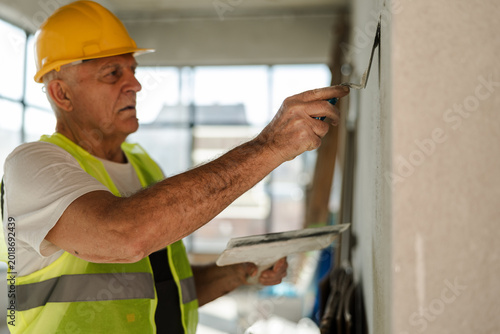 Senior Worker Applies Paint on a Wall in a Construction Site During the Day