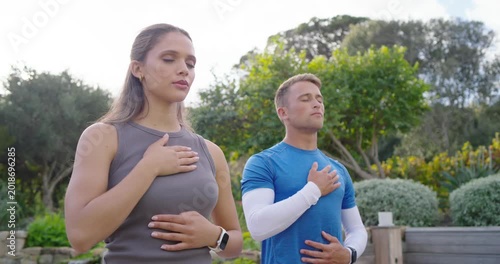 Fitness pair in sportswear following cue, hands on chest and belly, breathing in garden, smartwatch