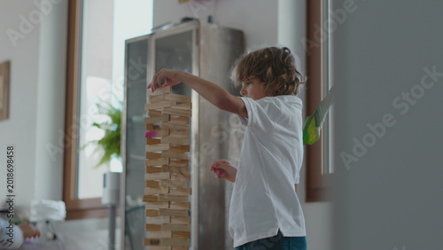 Tableau sur toile Boy standing beside tall wooden block tower adding pieces with calm concentratio