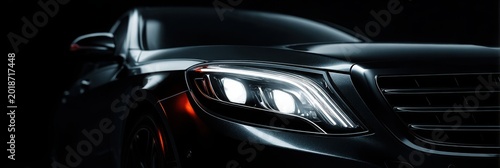 Close-up of a modern black luxury car with illuminated LED headlight in dramatic dark lighting and sleek automotive design.