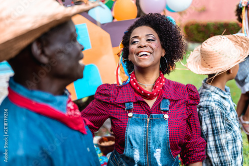 Happy Black woman celebrating Festa Junina traditional Brazilian June festival with family outdoors.