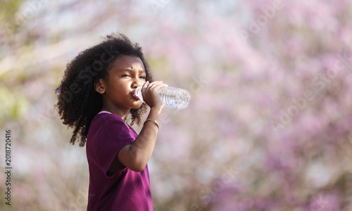 A child drinking water outdoors in a natural environment. Concept of hydration, healthy lifestyle, wellness, childhood health, and refreshing outdoor activity.