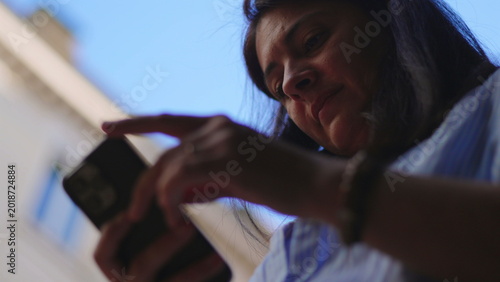 Woman holding smartphone outside while tapping and swiping screen with focused expression creating relaxed moment of digital engagement connection and everyday interaction