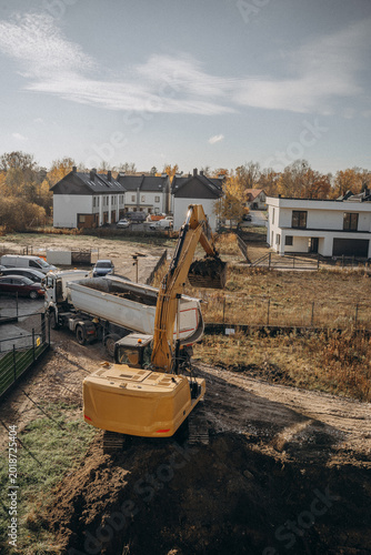 Orange excavator digging a foundation pit for residential building construction.