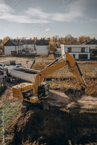 Orange excavator digging a foundation pit for residential building construction.